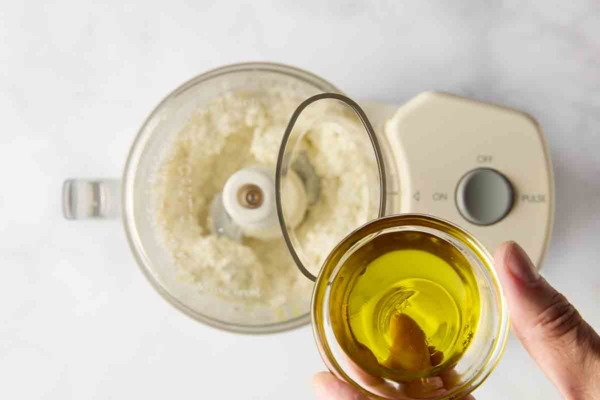 A person adding oil to a feta mixture in a food processor.