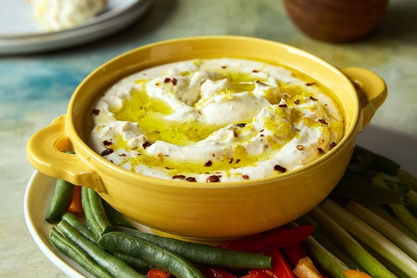 A bowl of whipped feta dip topped with oil and lemon zest on a platter of raw vegetables.