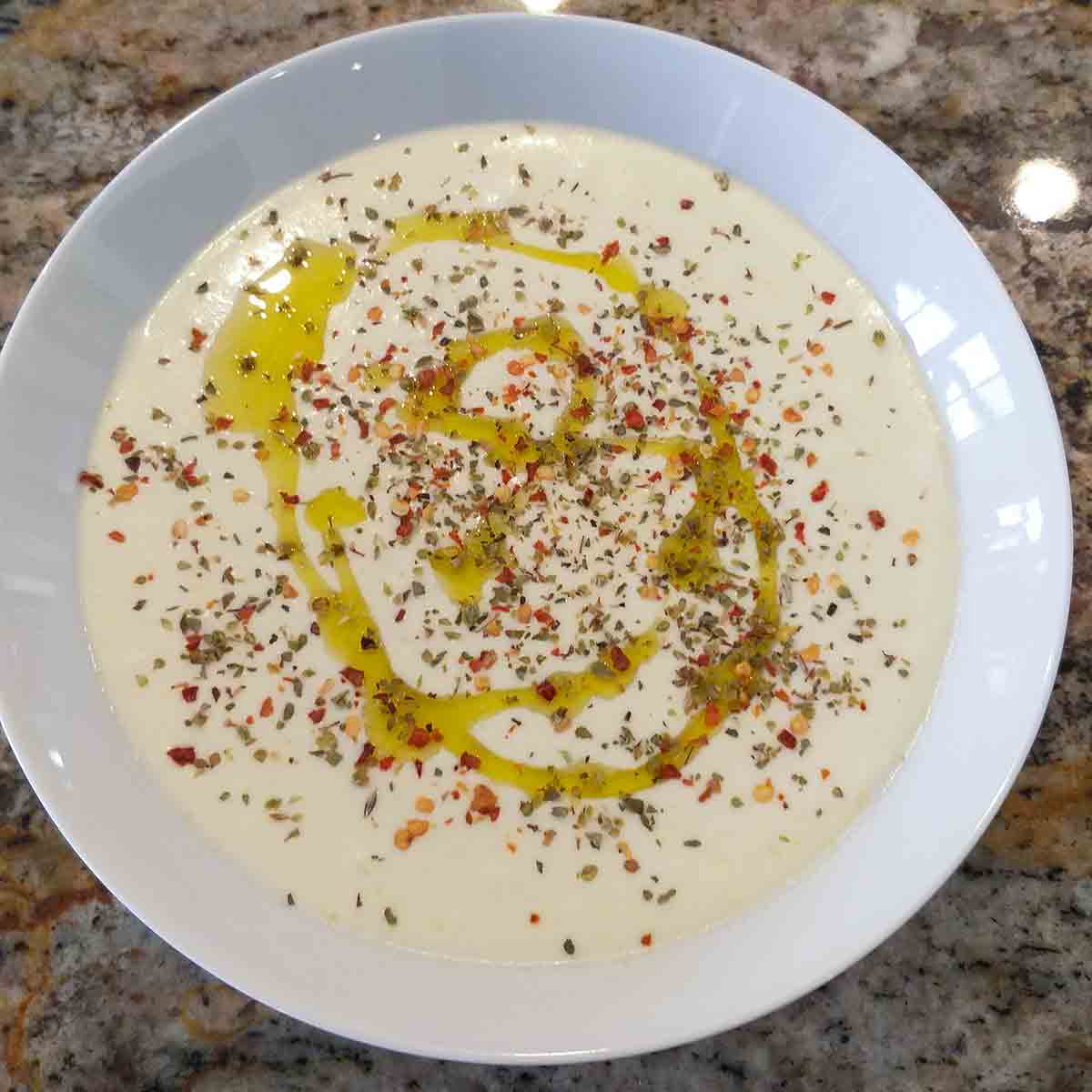 A white bowl filled with feta dip drizzled with oil and topped with spices.