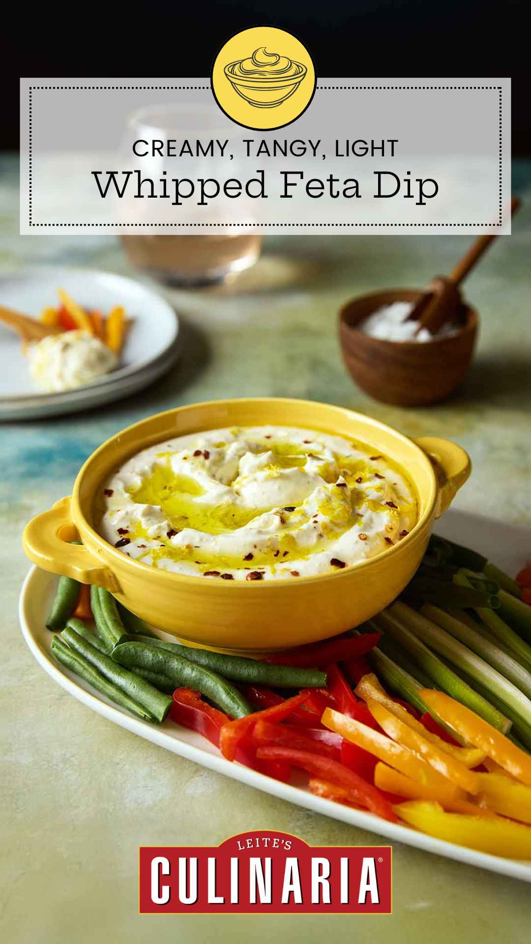 A bowl of whipped feta dip topped with oil and lemon zest on a platter of raw vegetables.