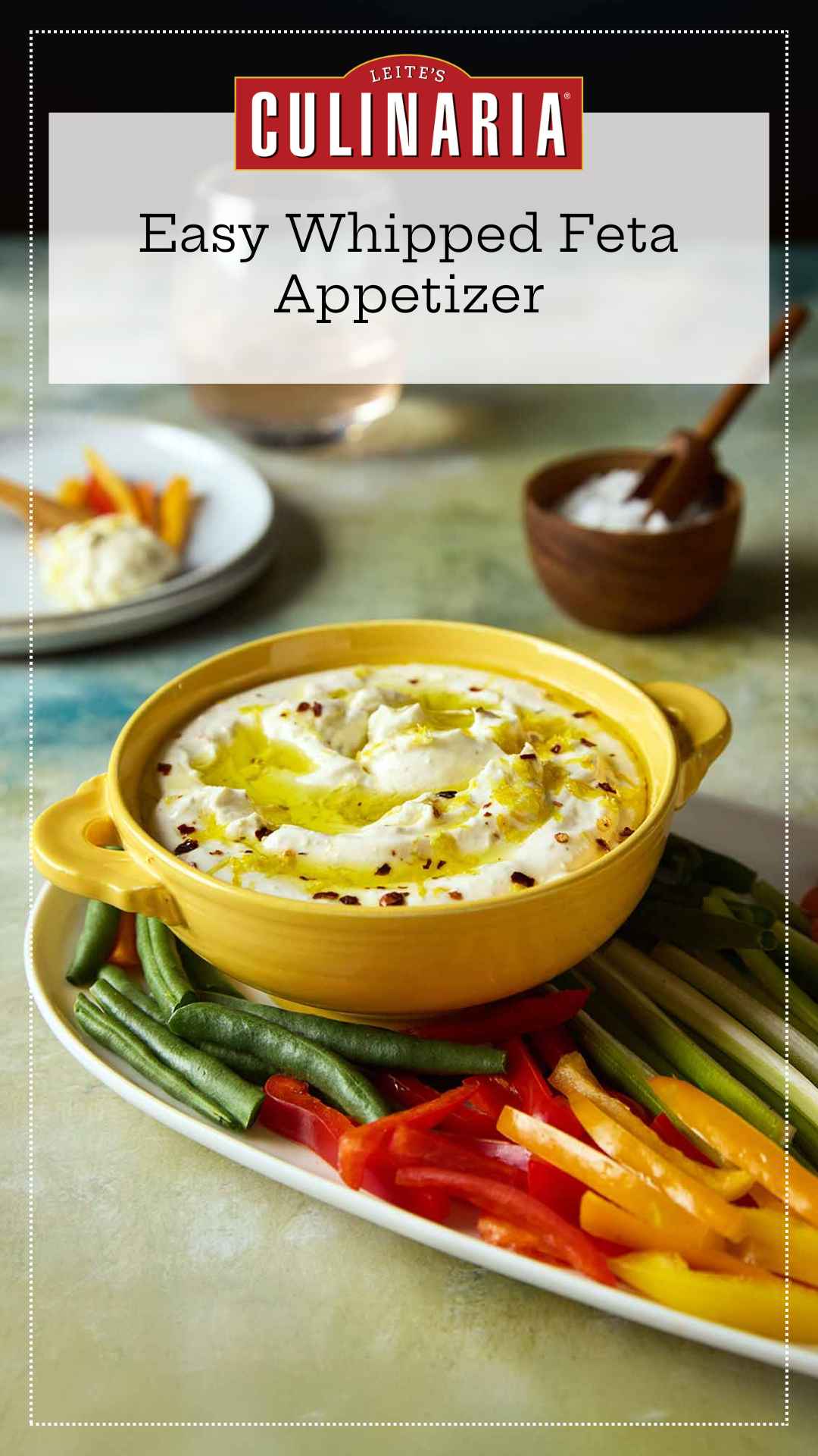 A bowl of whipped feta dip topped with oil and lemon zest on a platter of raw vegetables.