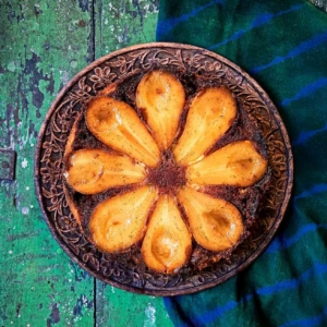 A pear and cardamom caramel upside-down cake on a carved wooden plate, on a green wooden table.