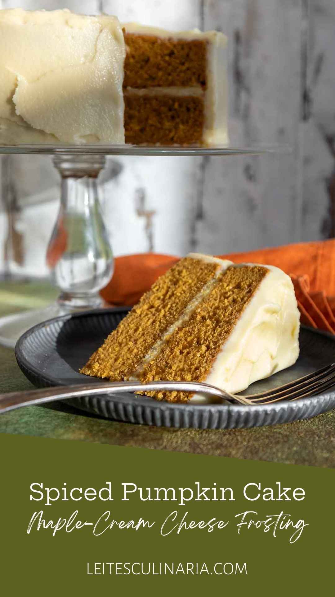 A slice of frosted pumpkin cake on a plate with the remaining cake on a stand in the background.