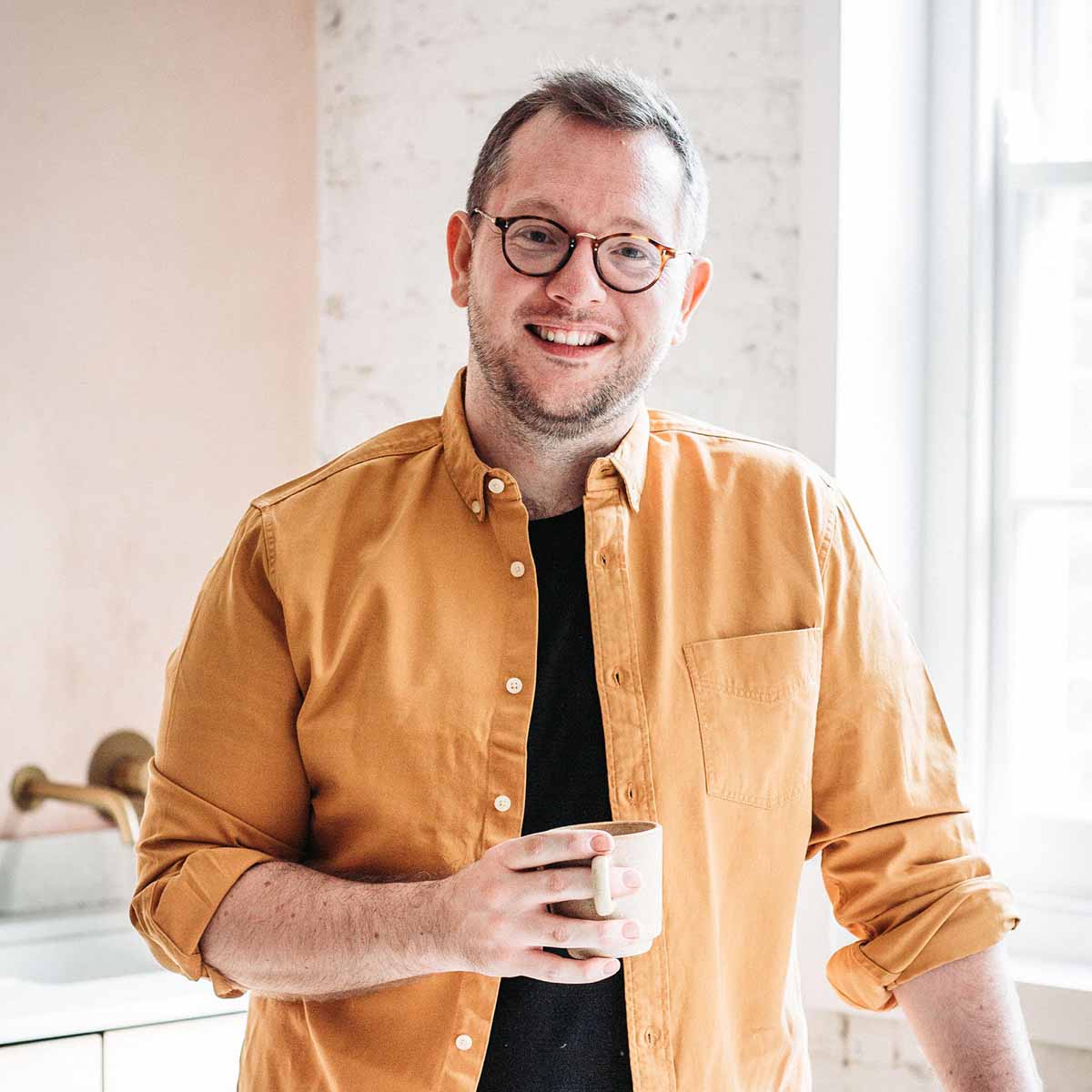 Edd Kimber leaning on a counter with a cup of coffee in his hand.