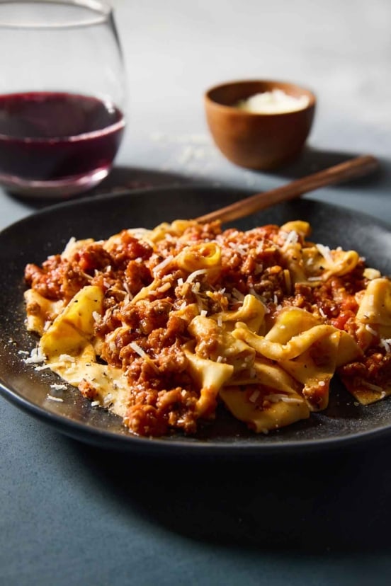 A black plate filled with Marcella Hazan's Bolognese sauce over homemade tagliatelle.