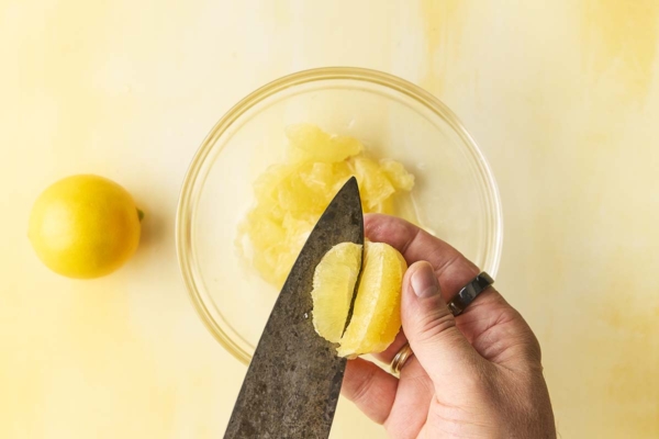 A man'a hand slicing into a Meyer lemon, separating the fruit from the membrane.