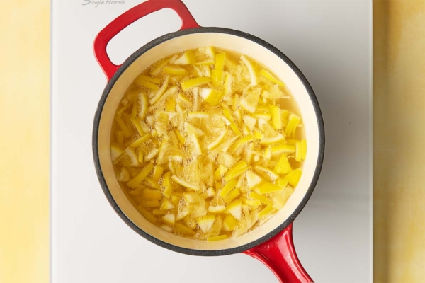 An overhead shot of a red pot filled with sliced Meyer lemons simmering in water.