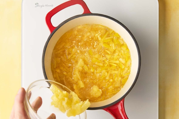 A man's hand dumping Meyer lemon slices into a pot of lemon pieces simmering in sugar water.