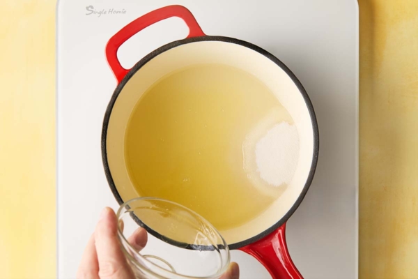 A man's hand pouring Meyer lemon juice into a pot of sugar and water.