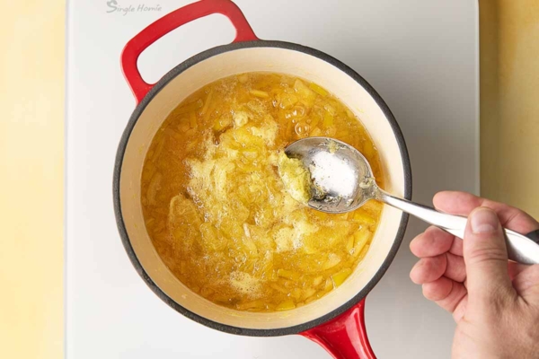 A man's hand skimming foam from a pot of simmering Meyer lemon marmalade.