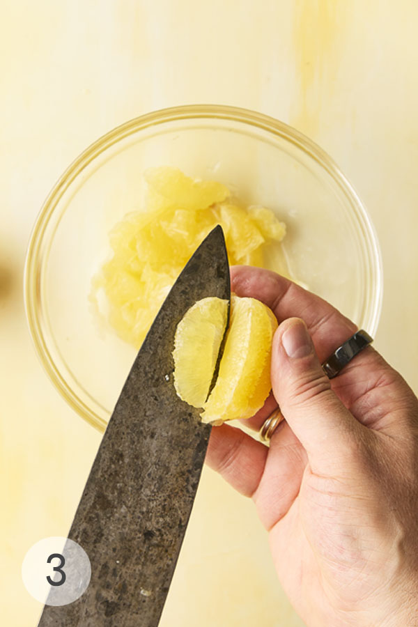 A man'a hand slicing into a Meyer lemon, separating the fruit from the membrane.