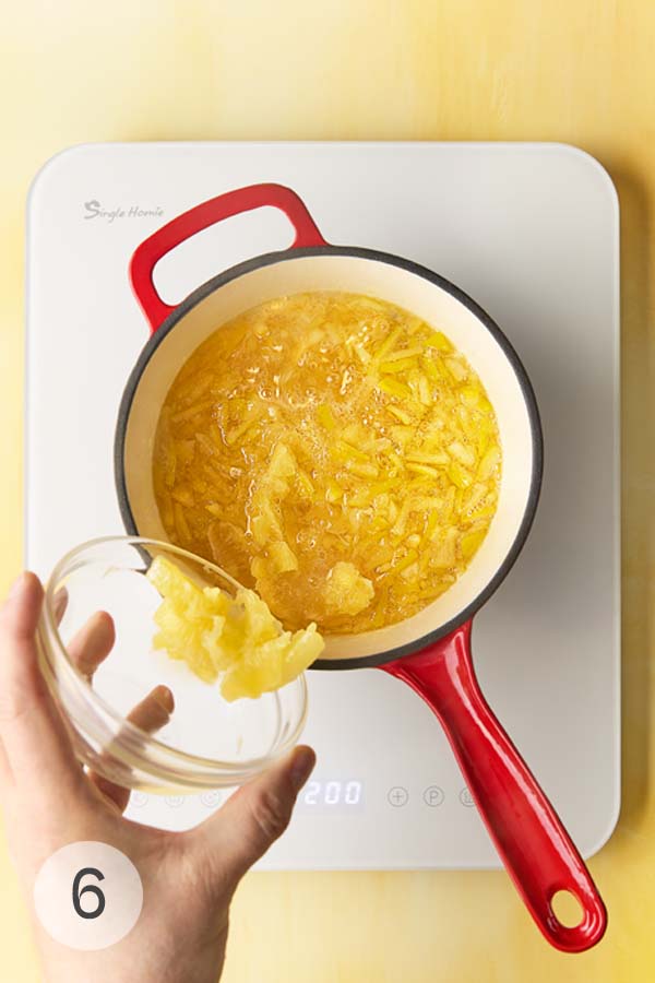 A man's hand dumping Meyer lemon slices into a pot of lemon pieces simmering in sugar water.