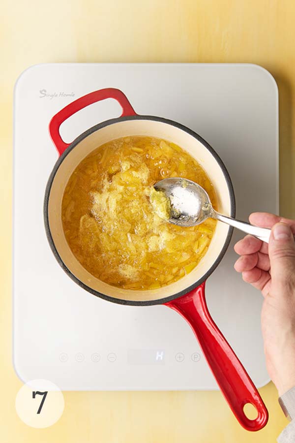 A man's hand skimming foam from a pot of simmering Meyer lemon marmalade.