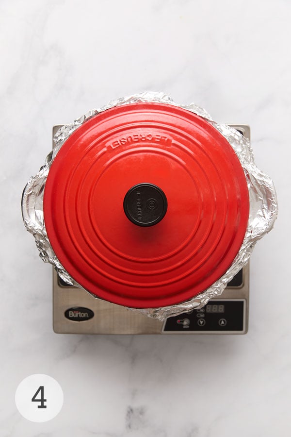 A red Dutch oven covered with foil and a lid.