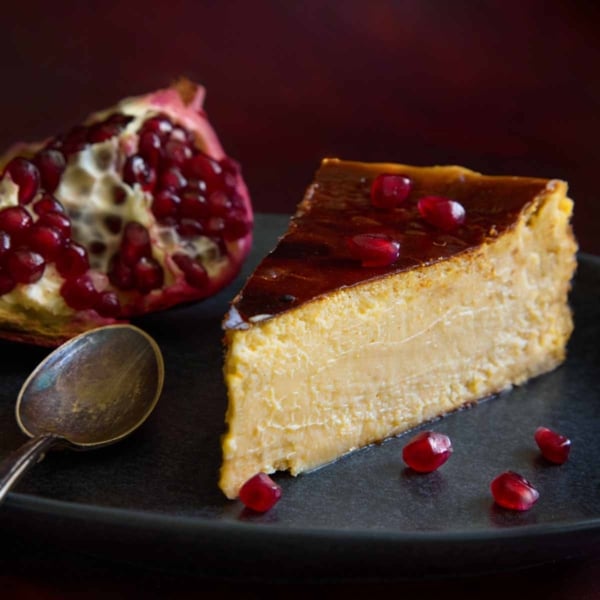 A slice of burnt Basque cheesecake with pomegranate, ready to be enjoyed.