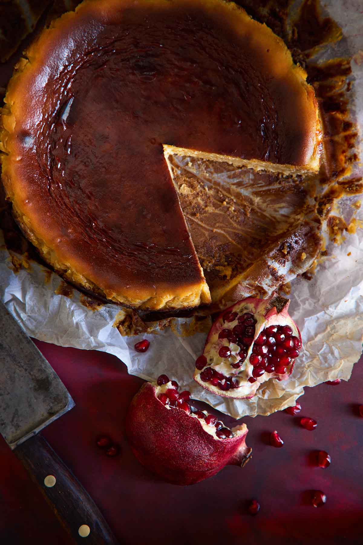 An overhead shot of a Basque Cheesecake with pomegranate, with a slice taken out to reveal the creamy interior.