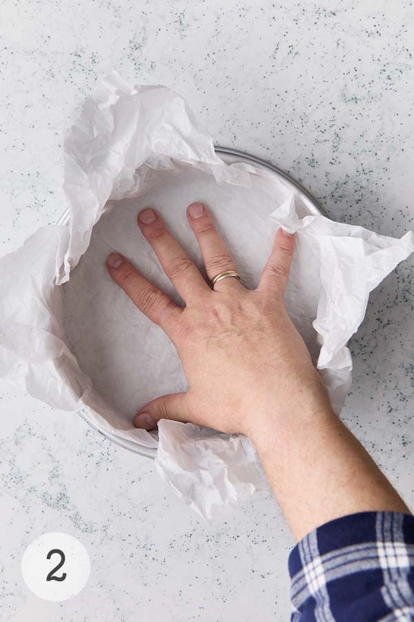 A man's hand pressing parchment paper into a pan for basque style cheesecake.