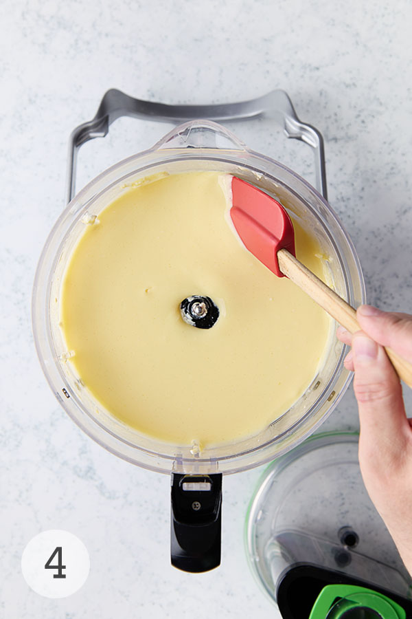 A man's hand scraping down the sides of a food processor fill with batter for blackened cheesecake.