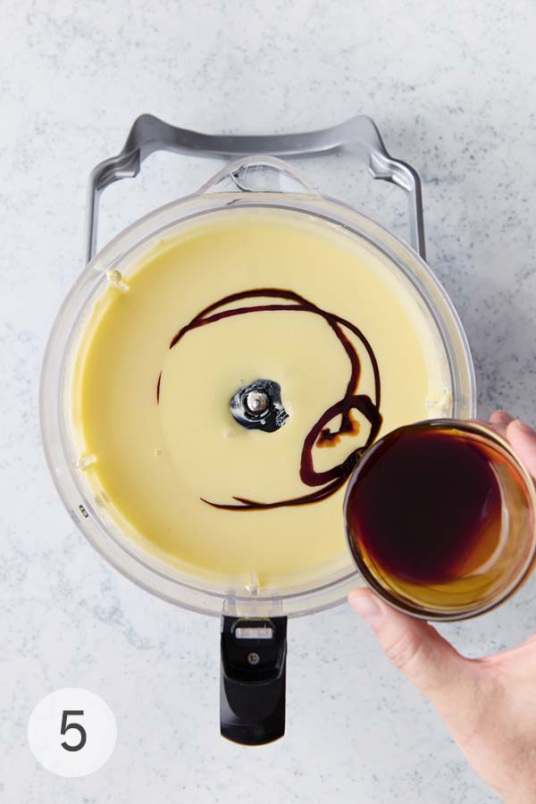 Pomegranate molasses being poured into a food processor filled with basque cheesecake recipe batter.