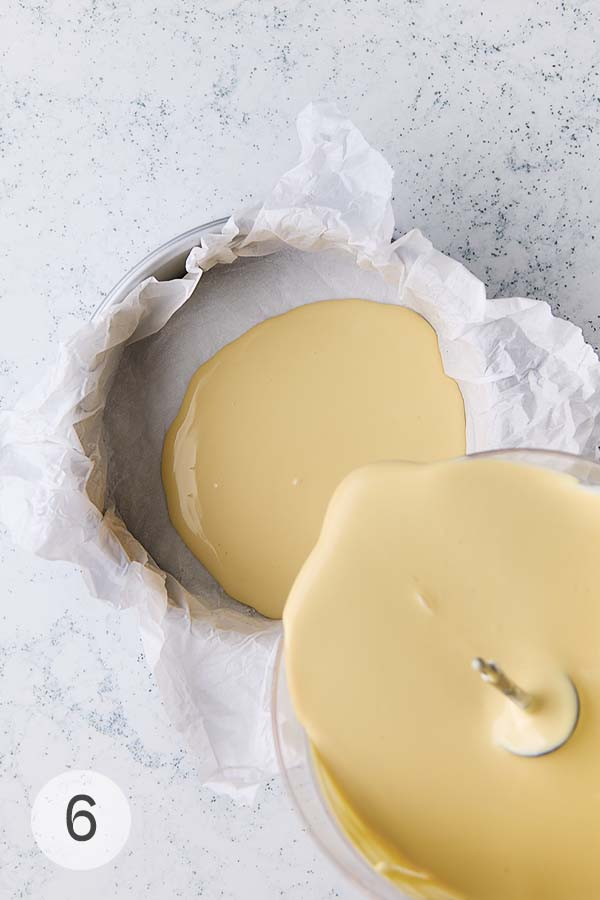 The batter for a burnt Basque cheesecake being poured into a springform pan lined with parchment paper.