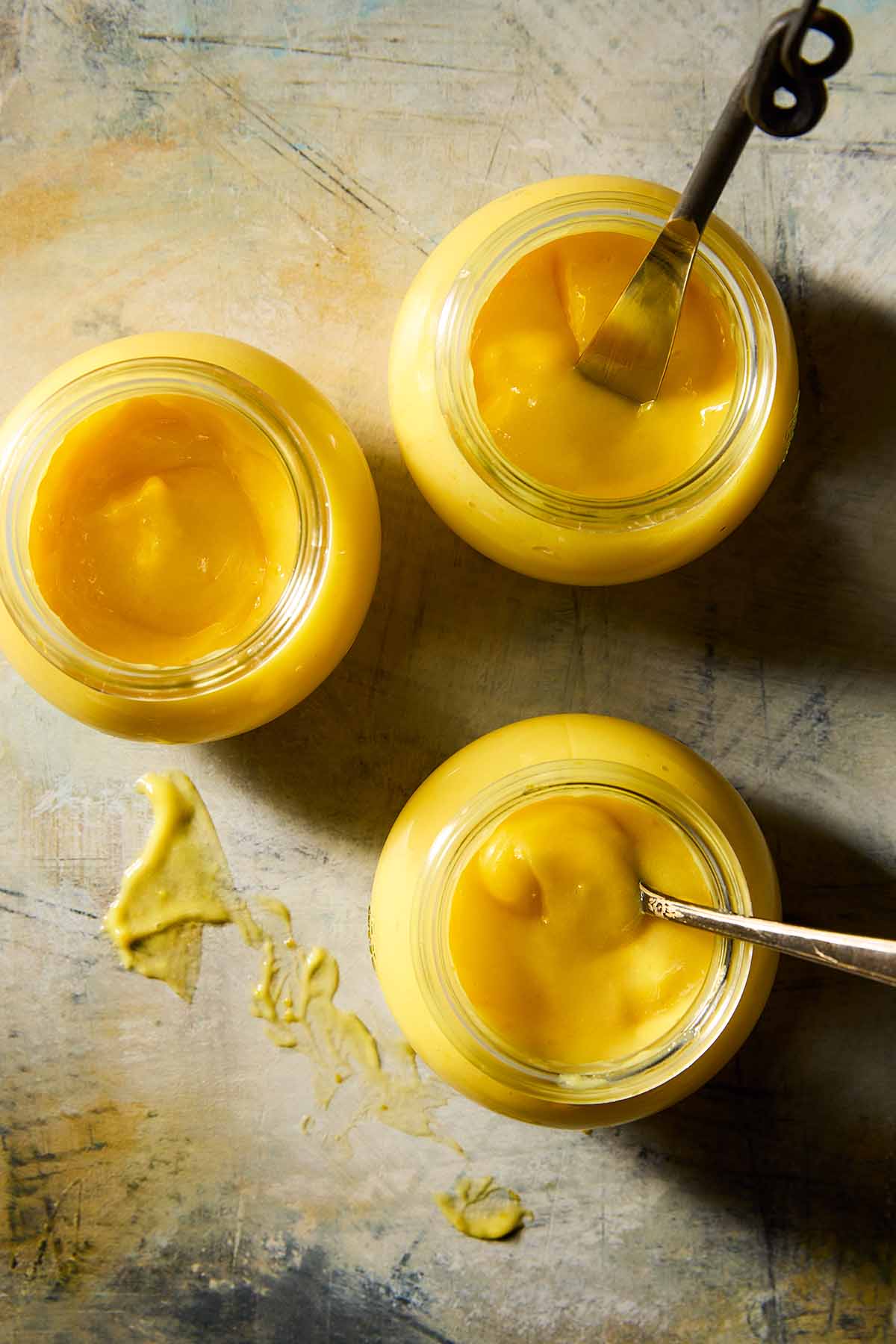 Three jars of homemade Meyer lemon curd, two with spoons in them.