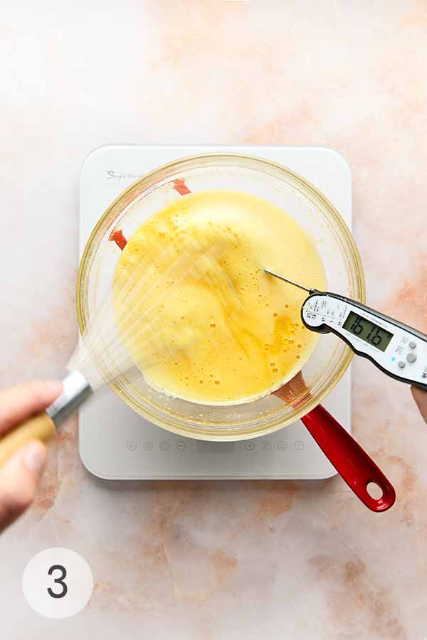 A man's hand whisking a bowl of uncooked Myhre lemon curd over a double boiler.