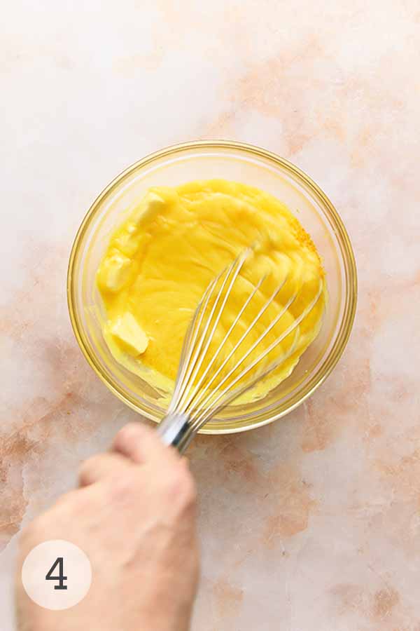 A man's hand whisking Meyer lemon curd, lemon zest, and butter together.