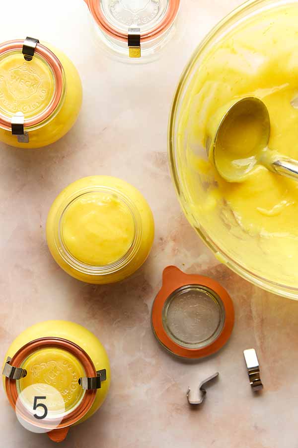 Jars of cooked my lemon curd; alongside is a large larger bowl and a ladle.