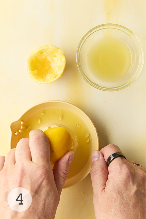 A man's handing juicing a Meyer lemon half. Nearby is a glass bowl of lemon juice.