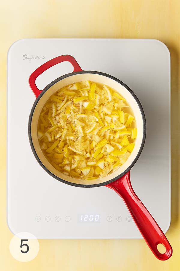 An overhead shot of a red pot filled with sliced Meyer lemons simmering in water.