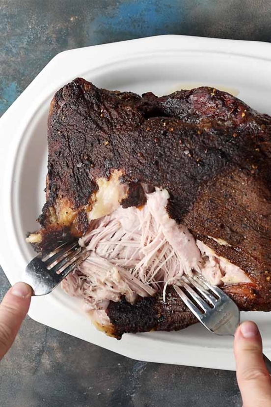 A man's shredding meat for pulled pork with two forks.