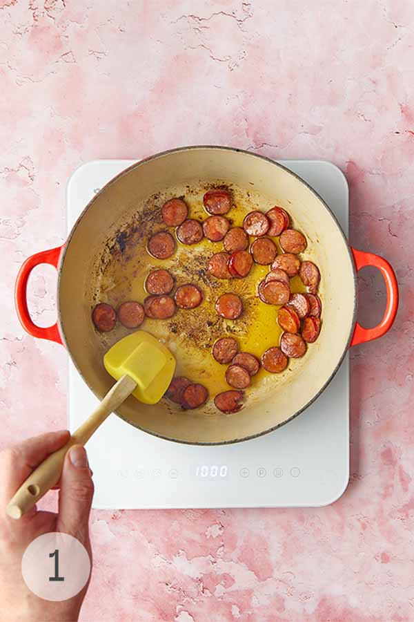 Slices of Portuguese sausage, chouriço, being stirred in a pot.