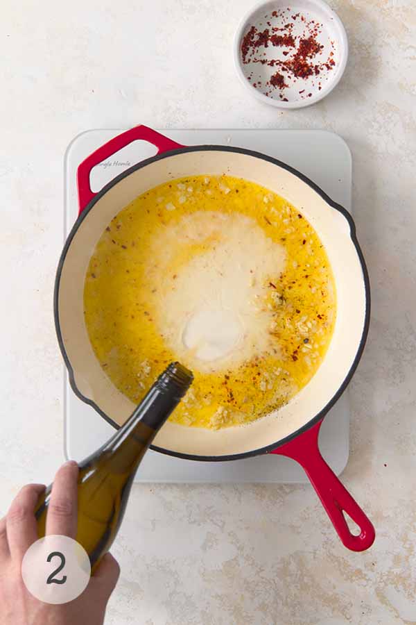 White wine being poured into a skillet of garlic butter, with red pepper flakes nearby, creating the flavorful base for shrimp scampi.