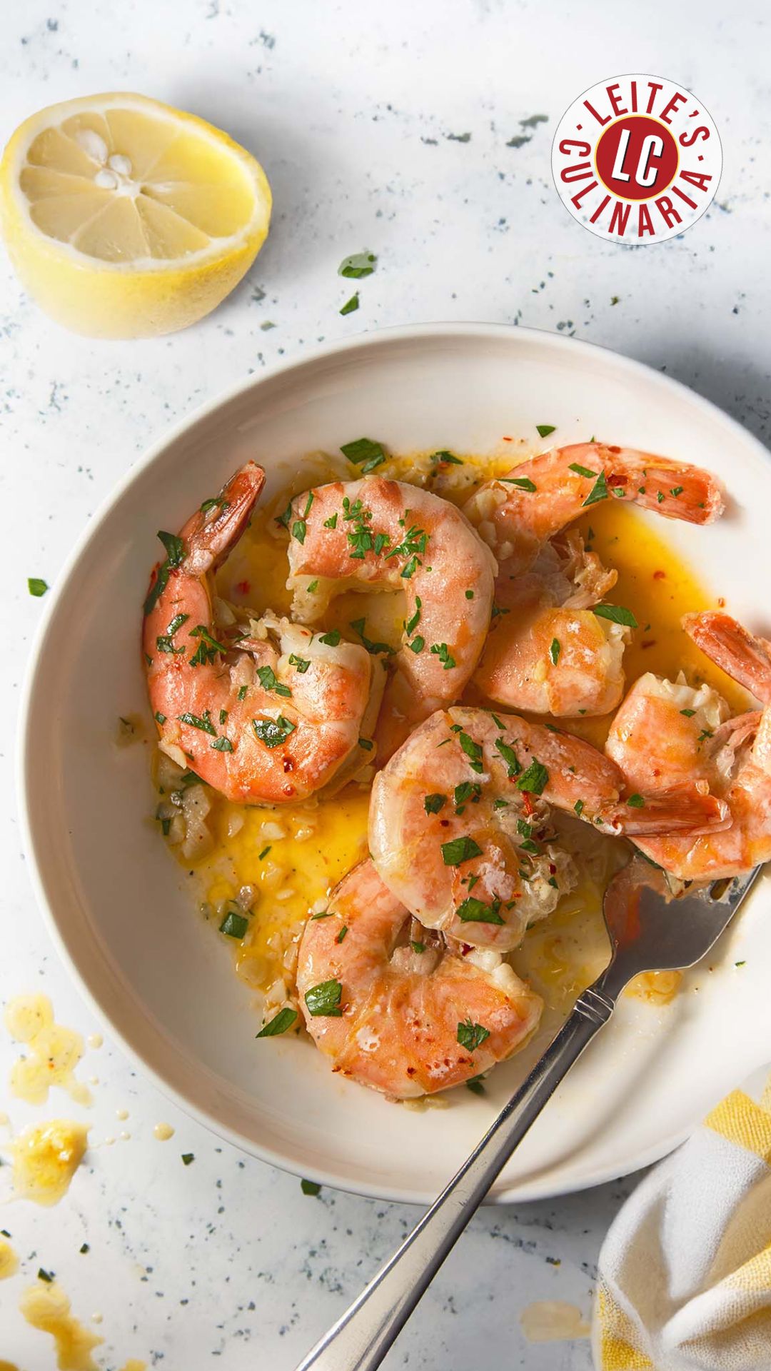 Overhead view of classic shrimp scampi in a garlic butter sauce, garnished with parsley, with a lemon wedge and a fork on the side.