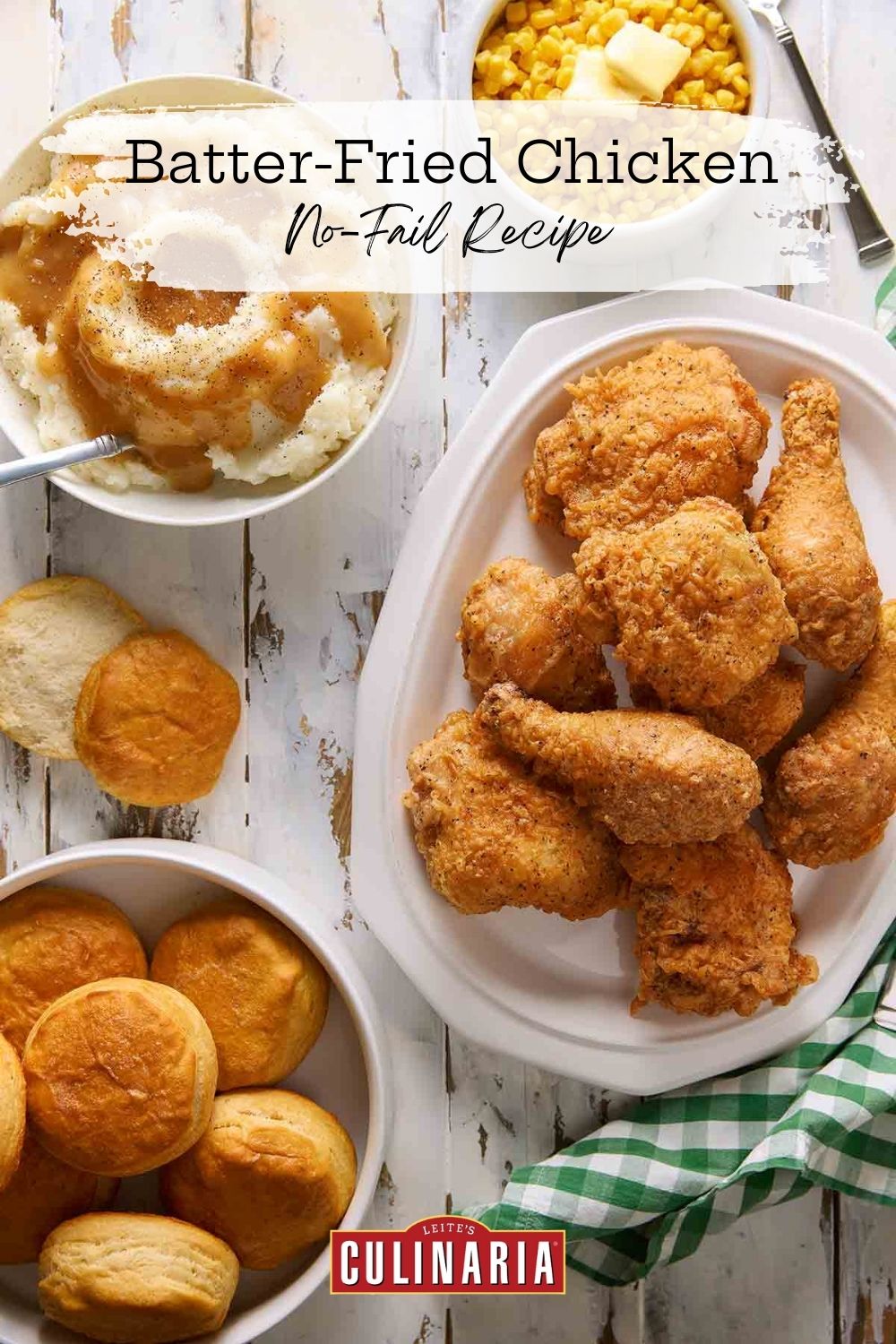 A platter of crispy batter-fried chicken with biscuits and mashed potatoes on a white table.