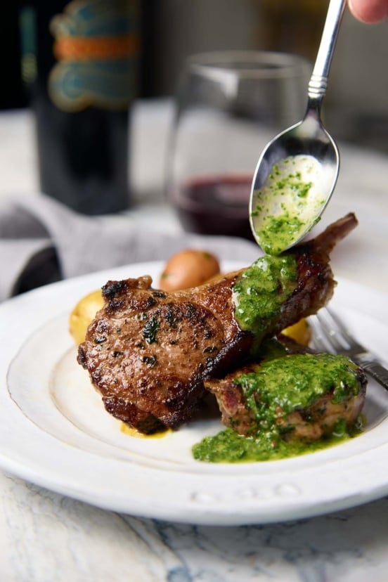 Pan-seared lamb chops drizzled with a vibrant green mint and cilantro sauce, served with potatoes.