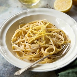Creamy lemon pasta with black pepper and lemon zest served in a white bowl with a green napkin and fork.