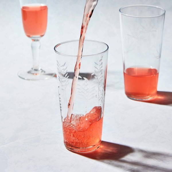 Pink rhubarb-infused vodka streaming from a pitcher into an etched glass filled with ice.
