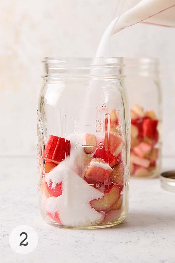 Granulated sugar being poured over chopped rhubarb in a mason jar.