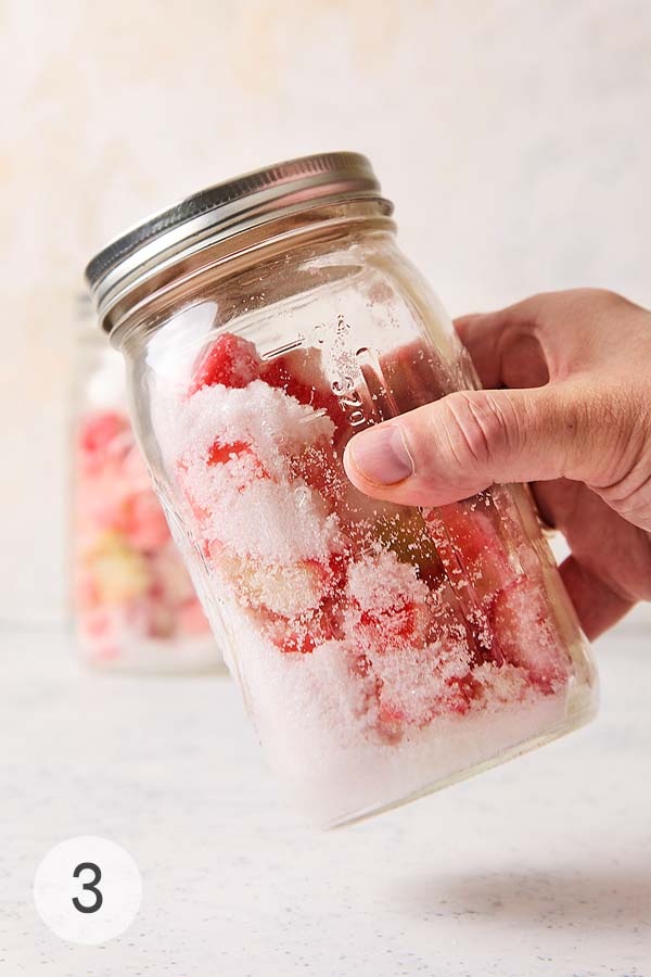 A hand shaking a mason jar of rhubarb and sugar to coat pieces evenly.