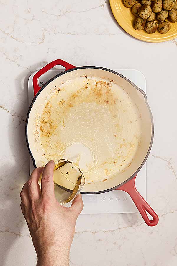 White wine poured into hot pan to deglaze after searing meatballs.