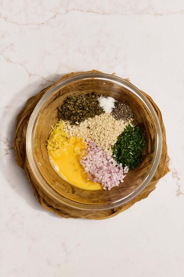 Shallots, capers, parsley, egg, lemon zest, and panko in a bowl for chicken piccata meatballs.