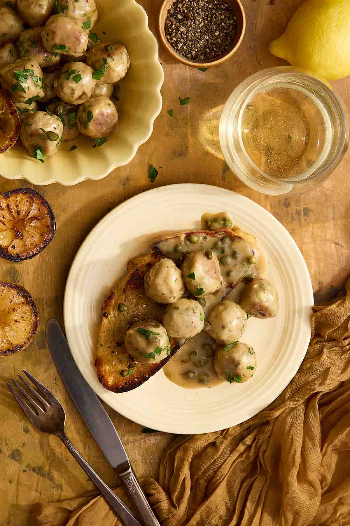 Chicken piccata meatballs on grilled sourdough with lemon and capers, served on a yellow plate with white wine.
