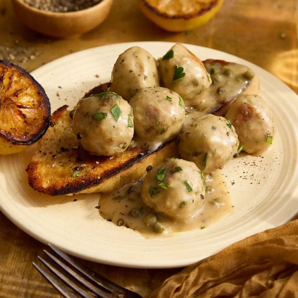 Square image of chicken meatballs with piccata sauce on grilled bread and a cream plate.
