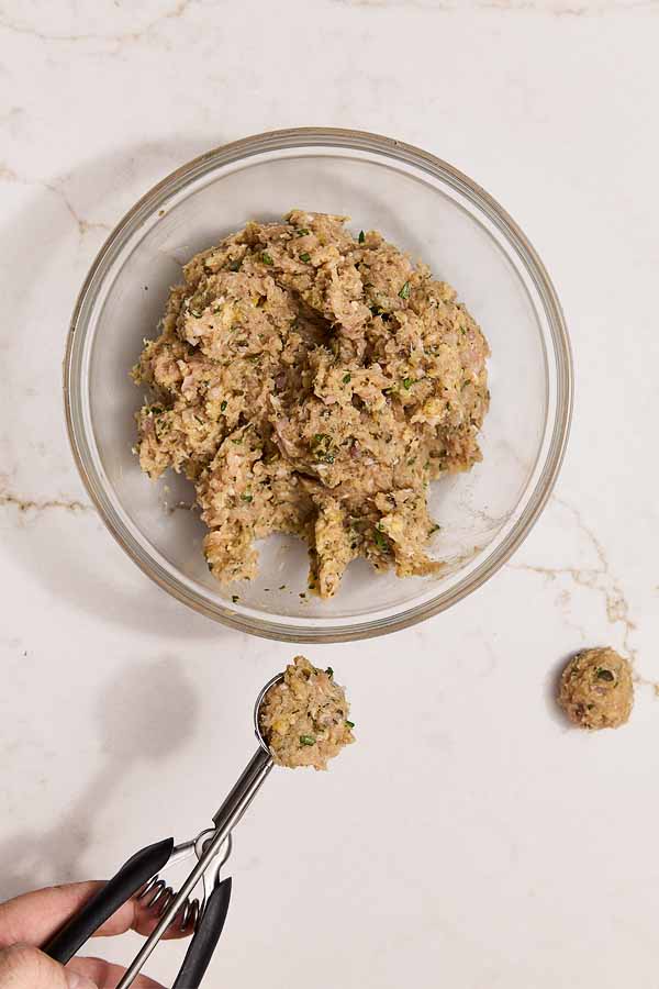 Ground chicken mixture being scooped into meatballs with a cookie scoop.
