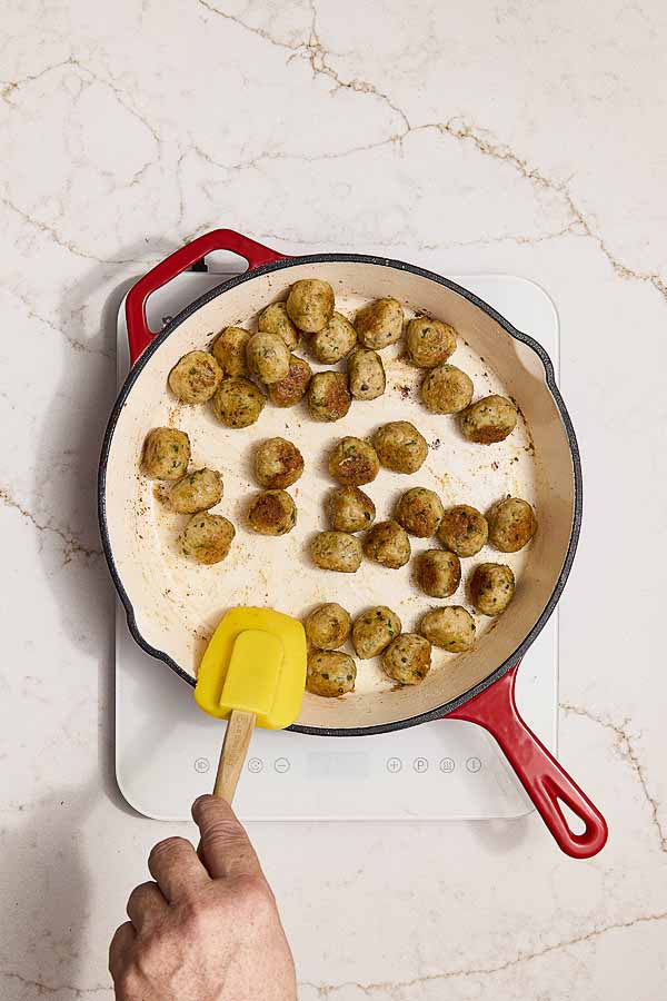 Chicken meatballs browning in a skillet to develop a golden crust.