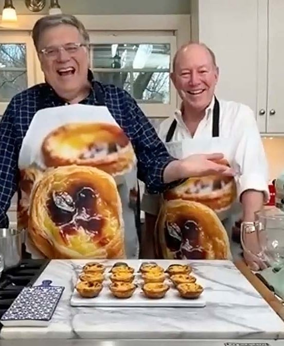 David Leite and Alan laughing in a kitchen behind a platter of freshly baked pastéis de nata for their Portuguese custard tarts masterclass.