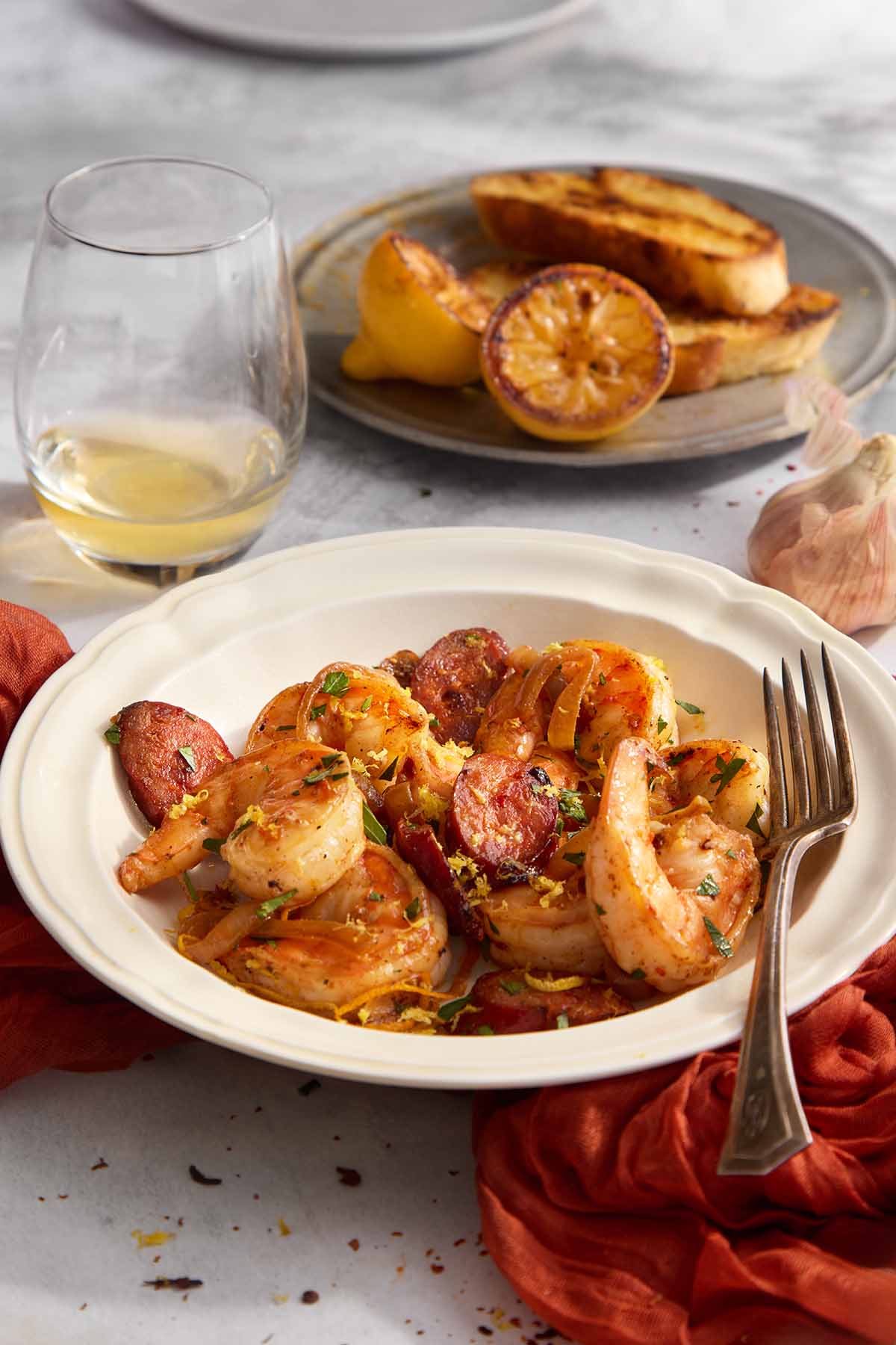 Shrimp and chorizo plated in a white bowl, topped with parsley and lemon zest, with grilled lemon halves beside the dish.