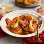 Cooked shrimp and chorizo garnished with parsley and lemon zest on a white plate.