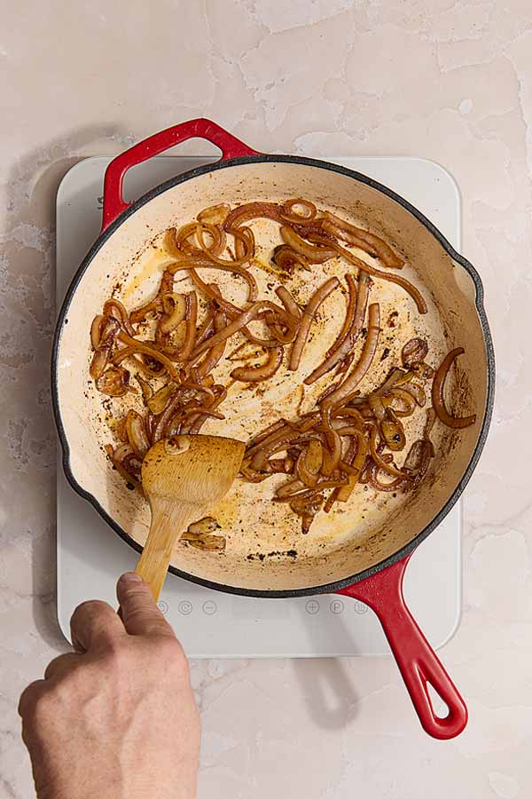 Sautéed onions softening and picking up color in a skillet with rendered chorizo (or chouriço) oil.